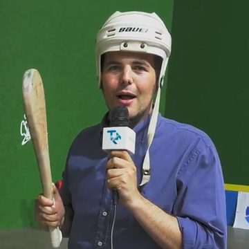 Carlos Villar como reportero de televisión en un trinquete, con casco y pala